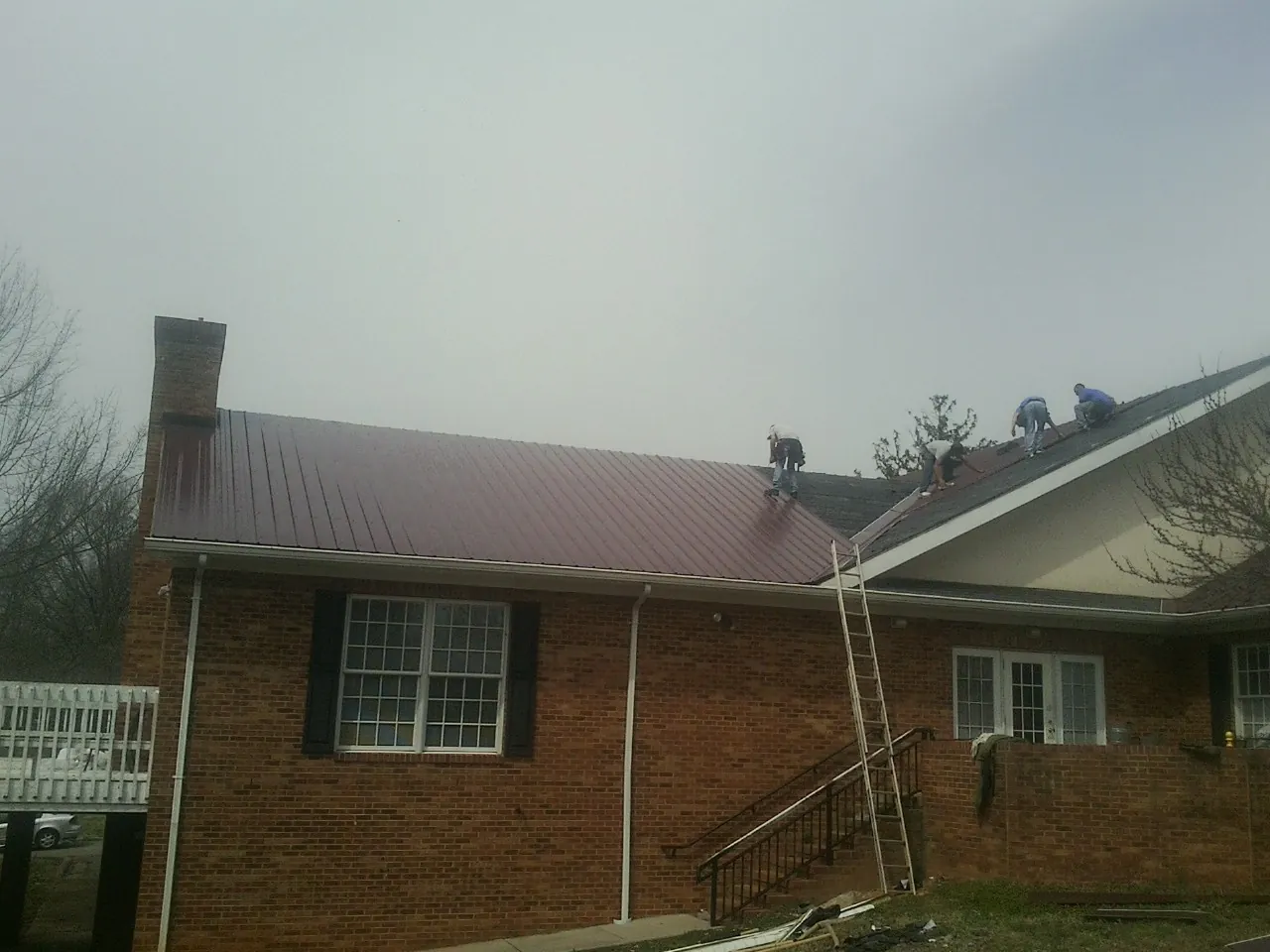 Crew setting red metal roofing panels on a brick home in Winterville