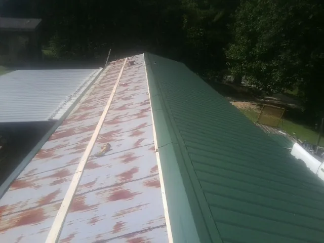 Old rusted panels beside newly installed green metal roofing — Wind Damage Roof Repair by Roofing Brothers in Winterville