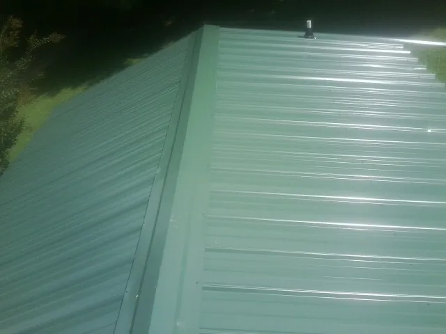 New green metal panels meeting at the ridge of a roof — Flat Roof Repair work by our crew in Winterville