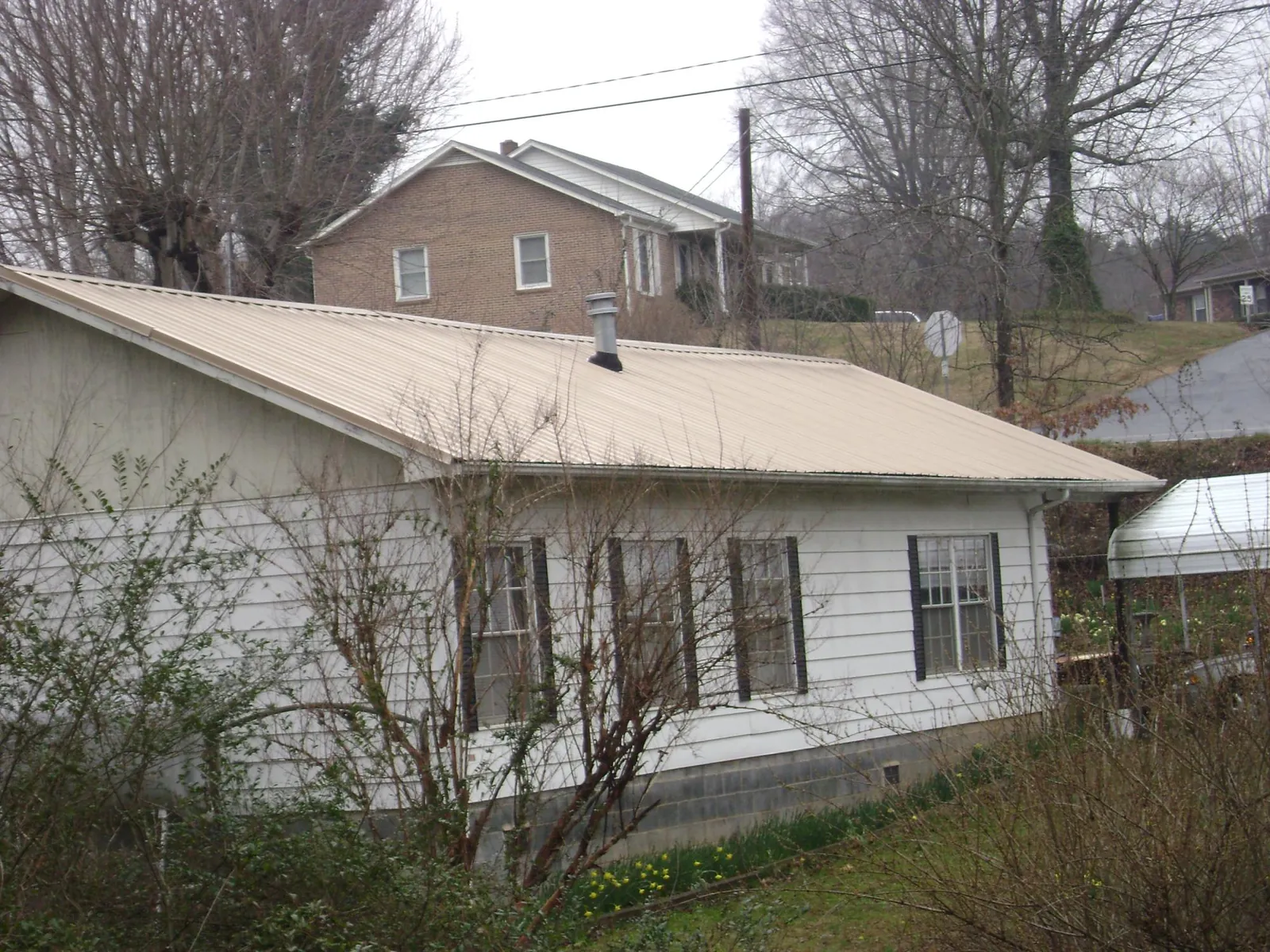 Tan metal roof on a white sided house set into a hillside — Commercial Roofing by Roofing Brothers in Winterville